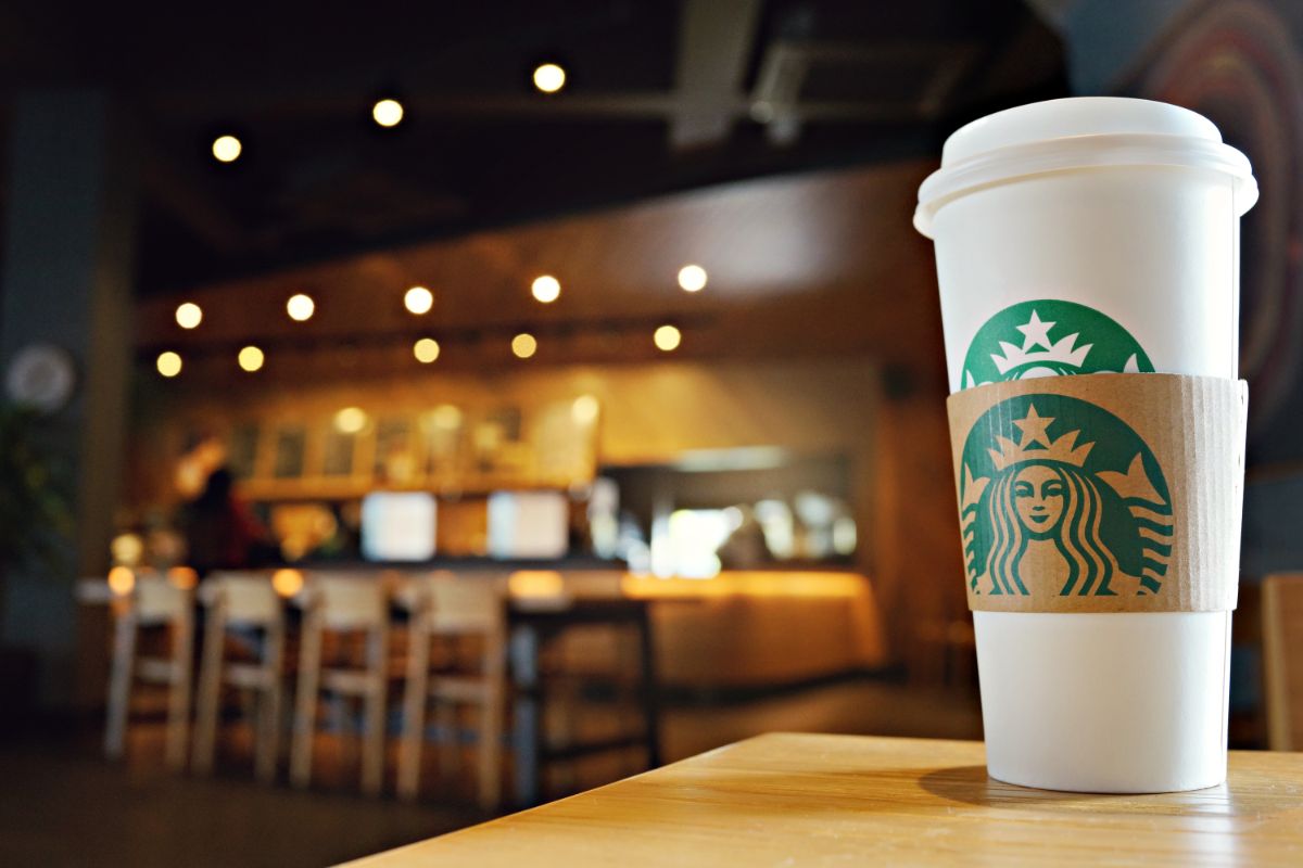 a starbucks takeaway cup sits in the foreground of a coffee shop