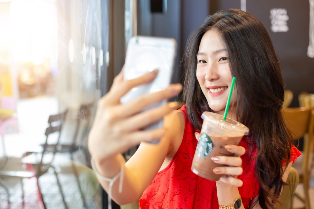an asian woman holds a starbucks drink up to her face while taking a selfie
