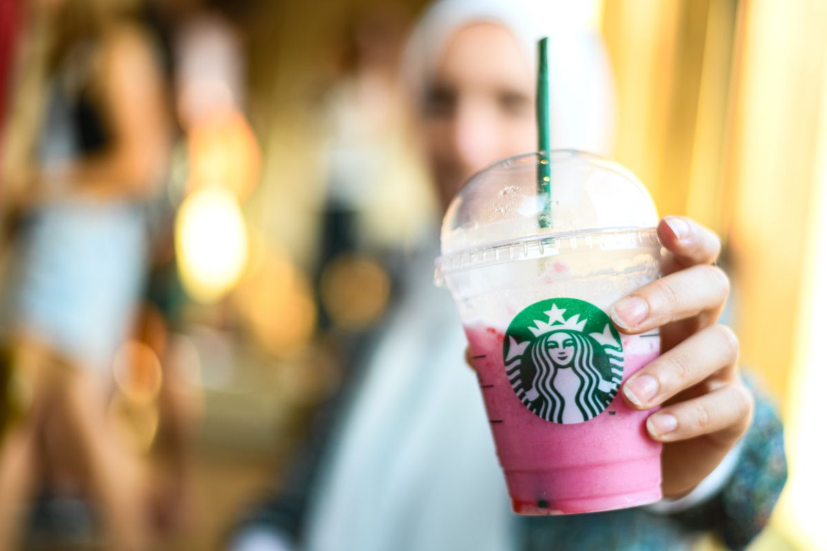 a woman blurred in the background holds a pink starbucks drink in front of her