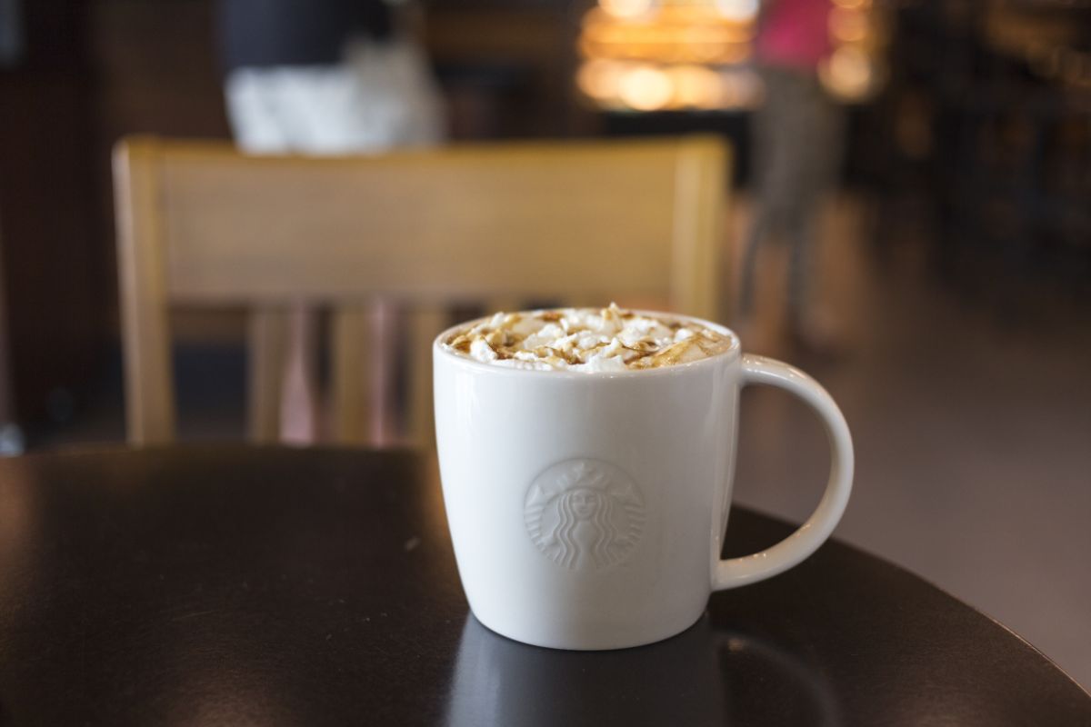 a starbucks mug sits on a table filled with a caramel drink topped with whipped cream and caramel drizzle
