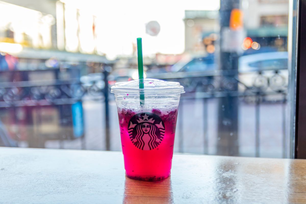 a Starbucks BHibiscus Berry Refresher sits on a table in front of a window through which a blurred city can be seen