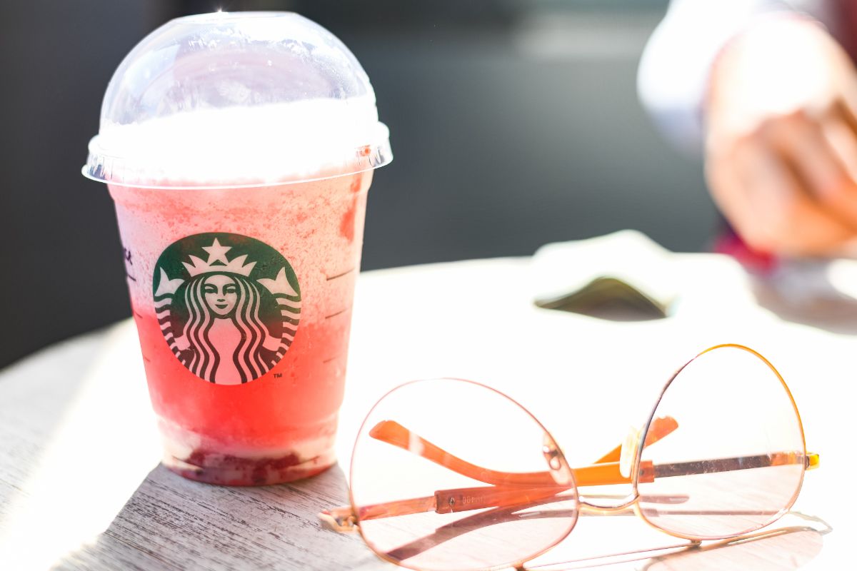 starbucks Refresher with a domed lid sits on a picnic table next to a pair of gold rimmed glasses