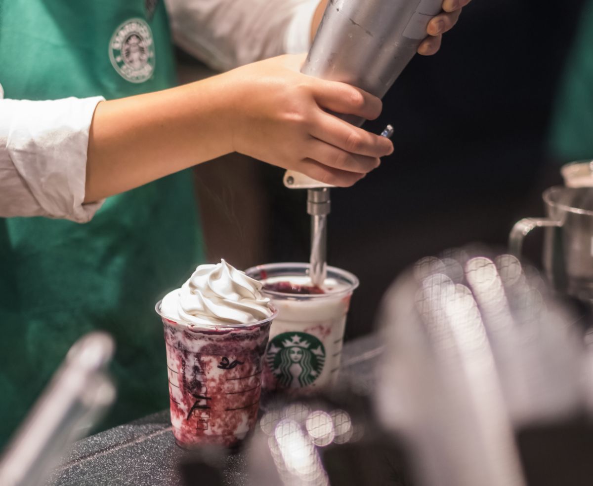 a Starbucks barista squirts cream onto the top of a cold drink